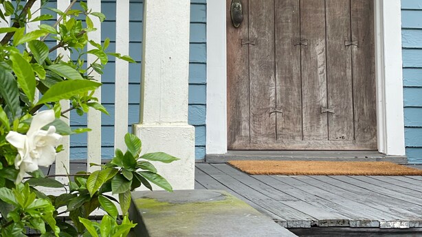 A wooden front door with a glass transom window, a white porch column, and a wooden deck. - The Painted Lady, a spacious renovated 4BR Victorian (St. Augustine)