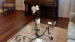 A living room with a piano, a chair, a coffee table with a vase of flowers, and a chandelier. - The Painted Lady, a spacious renovated 4BR Victorian (St. Augustine)