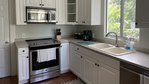 A kitchen with white cabinets, a stainless steel stove, a microwave, a coffee maker, and a window with a view of greenery. - The Painted Lady, a spacious renovated 4BR Victorian (St. Augustine)