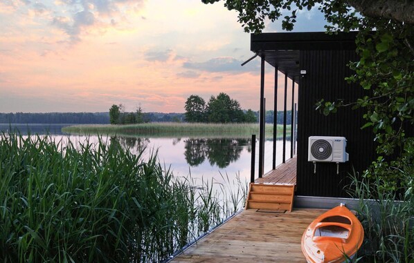 A wooden dock leading to a small cabin with a fan mounted on the exterior wall.
