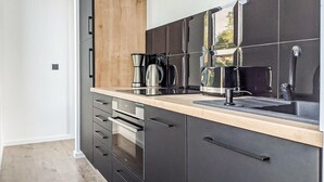 A modern kitchen with black cabinets, a wooden accent wall, and a stainless steel coffee maker.