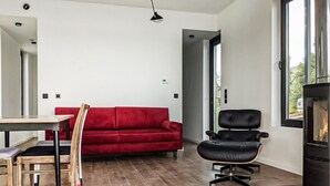 A modern living room with a red sofa, a black leather chair, a wooden dining table, and a fireplace.