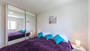 Ein Schlafzimmer mit einem großen Spiegel, einem Bett mit violetter Bettwäsche, zwei Nachttischen und einem an der Wand hängenden Bild.