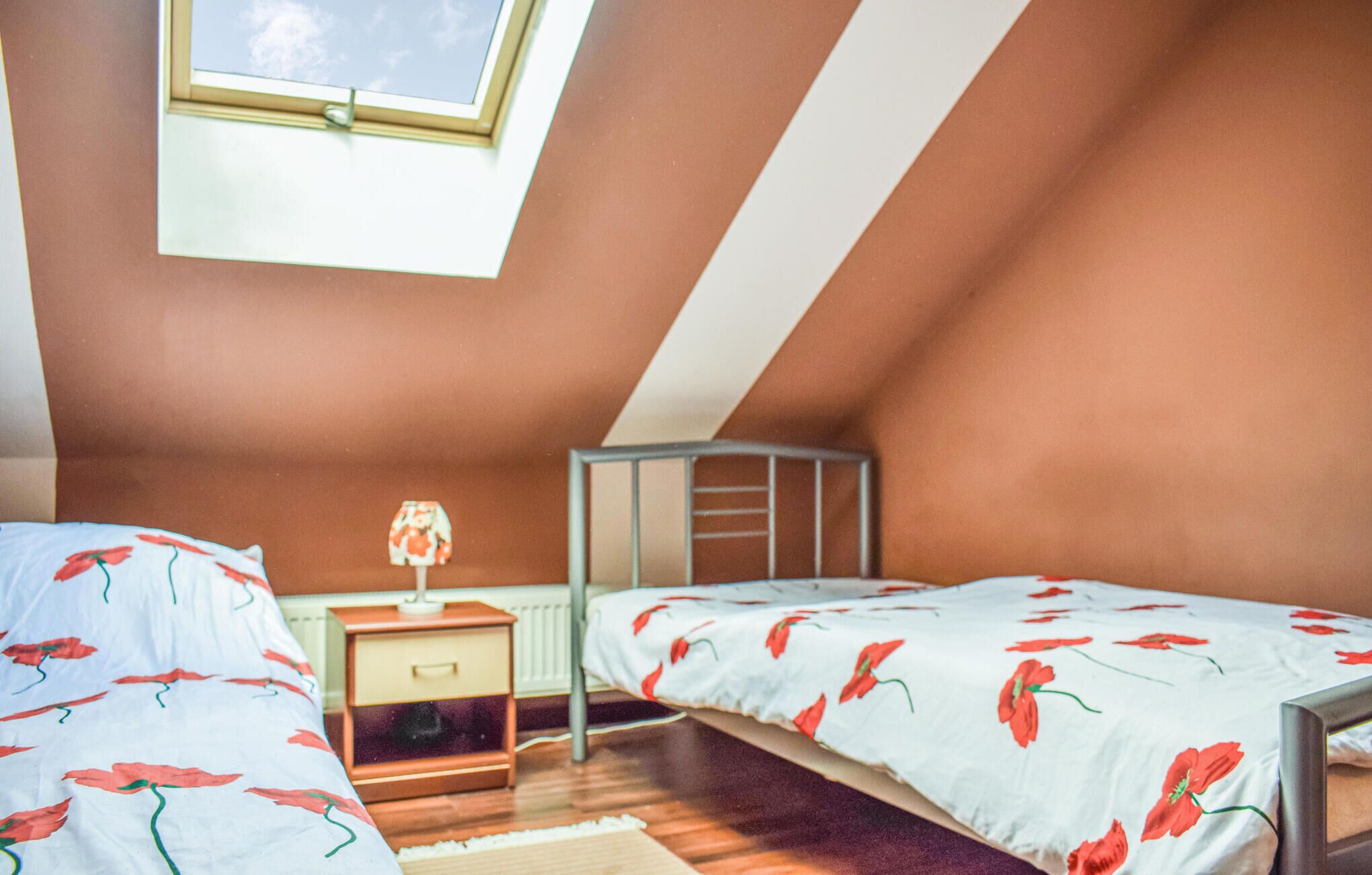 A small, cozy attic bedroom with two beds, a nightstand, and a window.