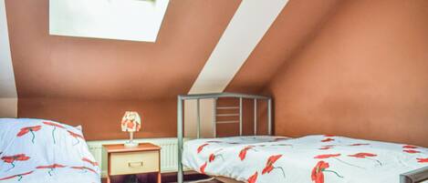 A small, cozy attic bedroom with two beds, a nightstand, and a window.