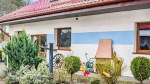 Ett hus med ett rött tegeltak, en blå rand på fasaden och en trädgård med olika växter och en väderkvarn.
