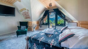 Ein gemütliches Schlafzimmer im Dachgeschoss mit Bett, Stuhl, Fernseher und Blick ins Freie.