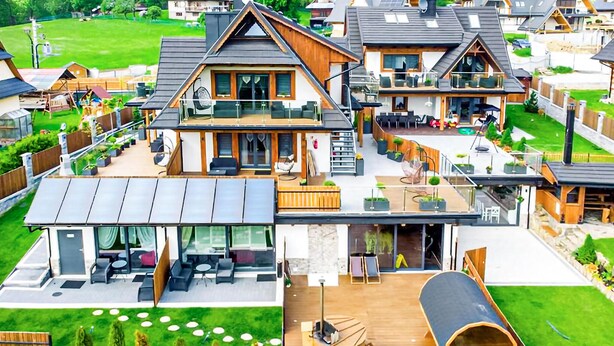 Ein moderner Wohnkomplex mit mehreren Häusern, jedes mit einem Balkon, Sitzgelegenheiten im Freien und einer großzügigen Terrassenfläche.