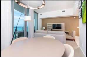 Une chambre d’hôtel moderne avec une table à manger ronde, un canapé, une télévision et un balcon avec vue.