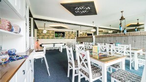 Un ristorante con sedie e tavoli bianchi, un muro decorato e un soffitto con motivo geometrico.