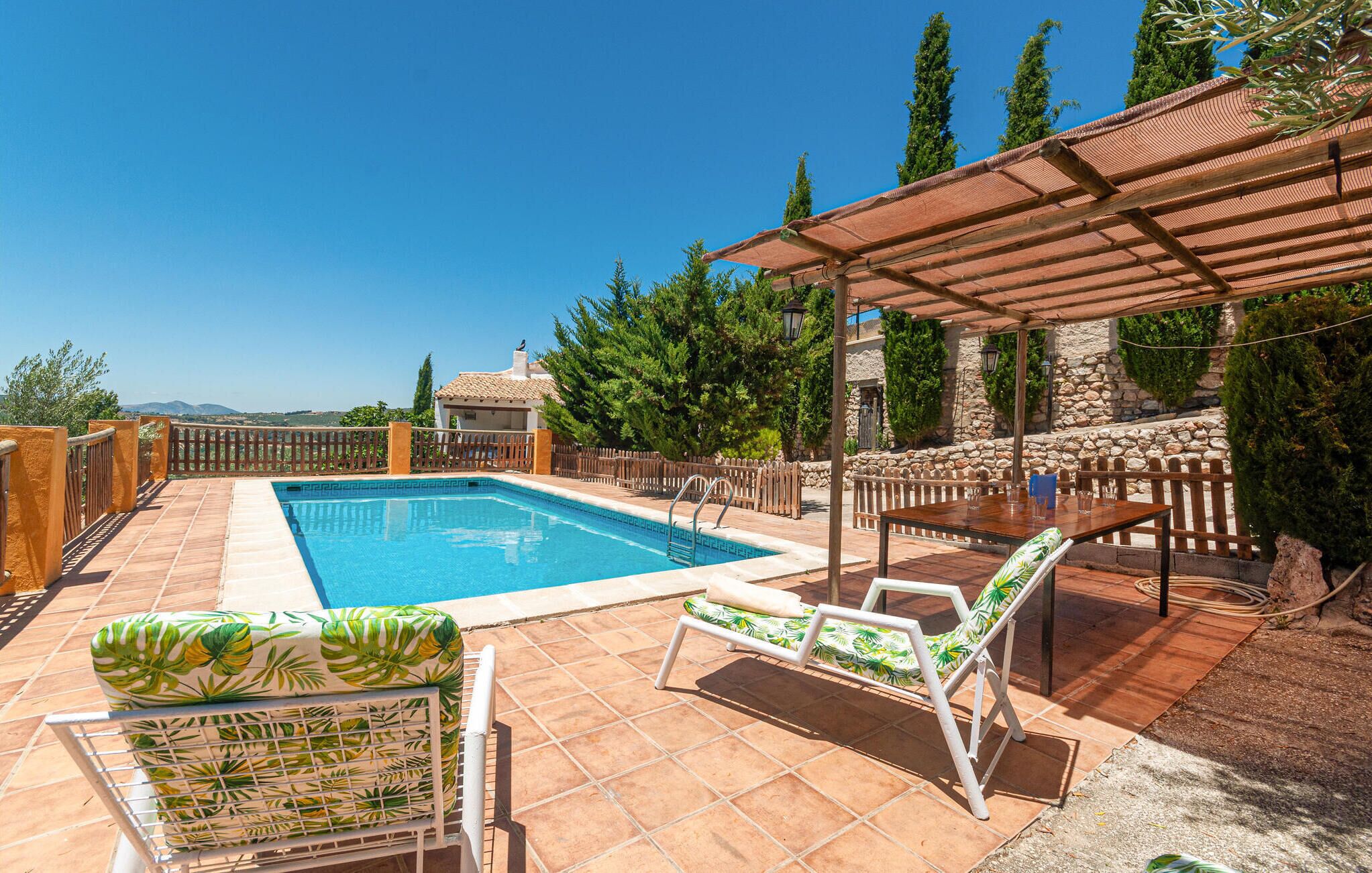 A swimming pool with lounge chairs and a pergola, surrounded by stone walls and greenery.