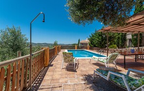 Zona de piscina amb una terrassa de fusta, gandules i una pèrgola.