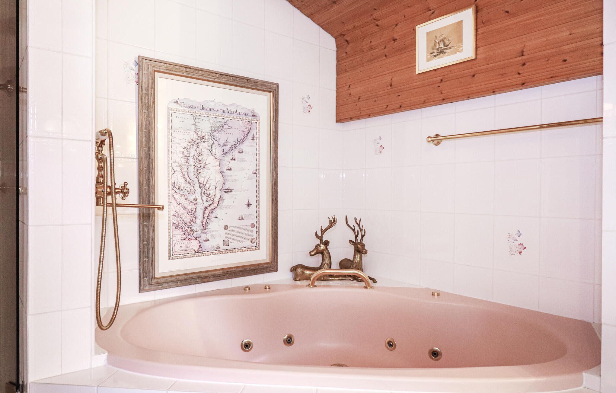 Une salle de bain avec une grande baignoire, une carte encadrée au mur et deux décorations représentant des têtes de cerf.