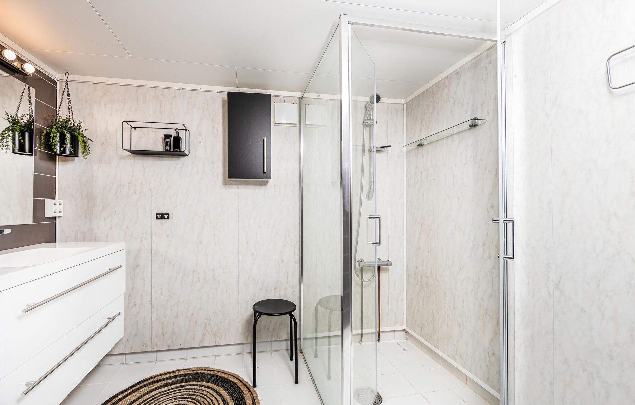 A modern bathroom with a glass shower enclosure, a white vanity with a mirror, and a small stool.