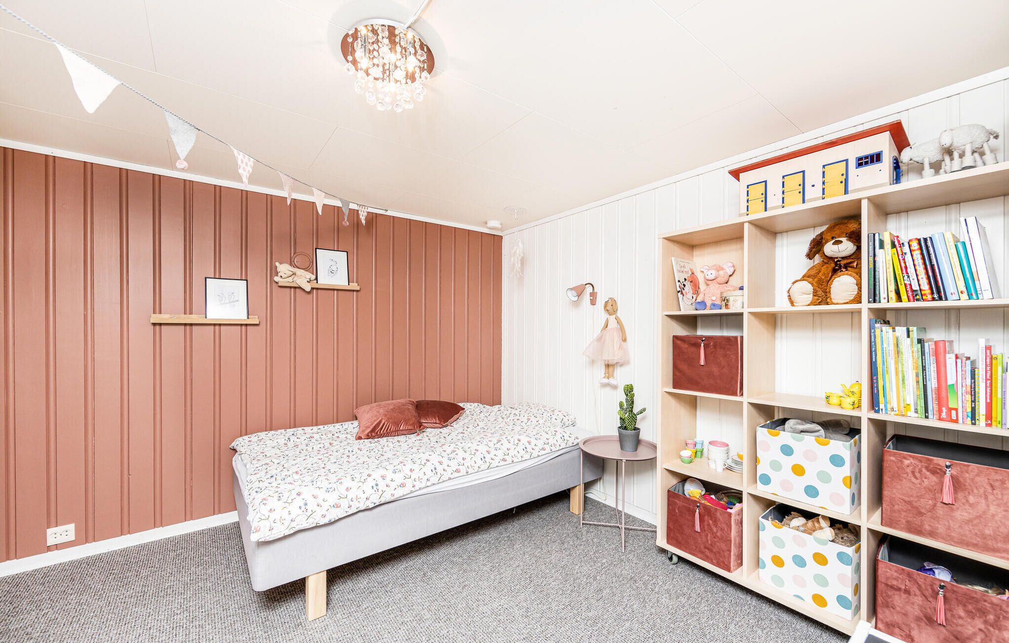 Ein Schlafzimmer mit einem Bett, einem kleinen Nachttisch, einem Bücherregal und einer Wandleuchte.