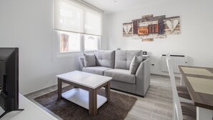 Ett modernt vardagsrum med en grå soffa, ett vitt soffbord, en tv och ett element.