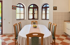 A dining area with a round table, six chairs, and three arched windows with curtains. - 4 bedroom amazing home in Sukosan (Sukosan)