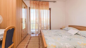 Quarto com cama, cadeira, guarda-roupa e janela com cortinas leves.
