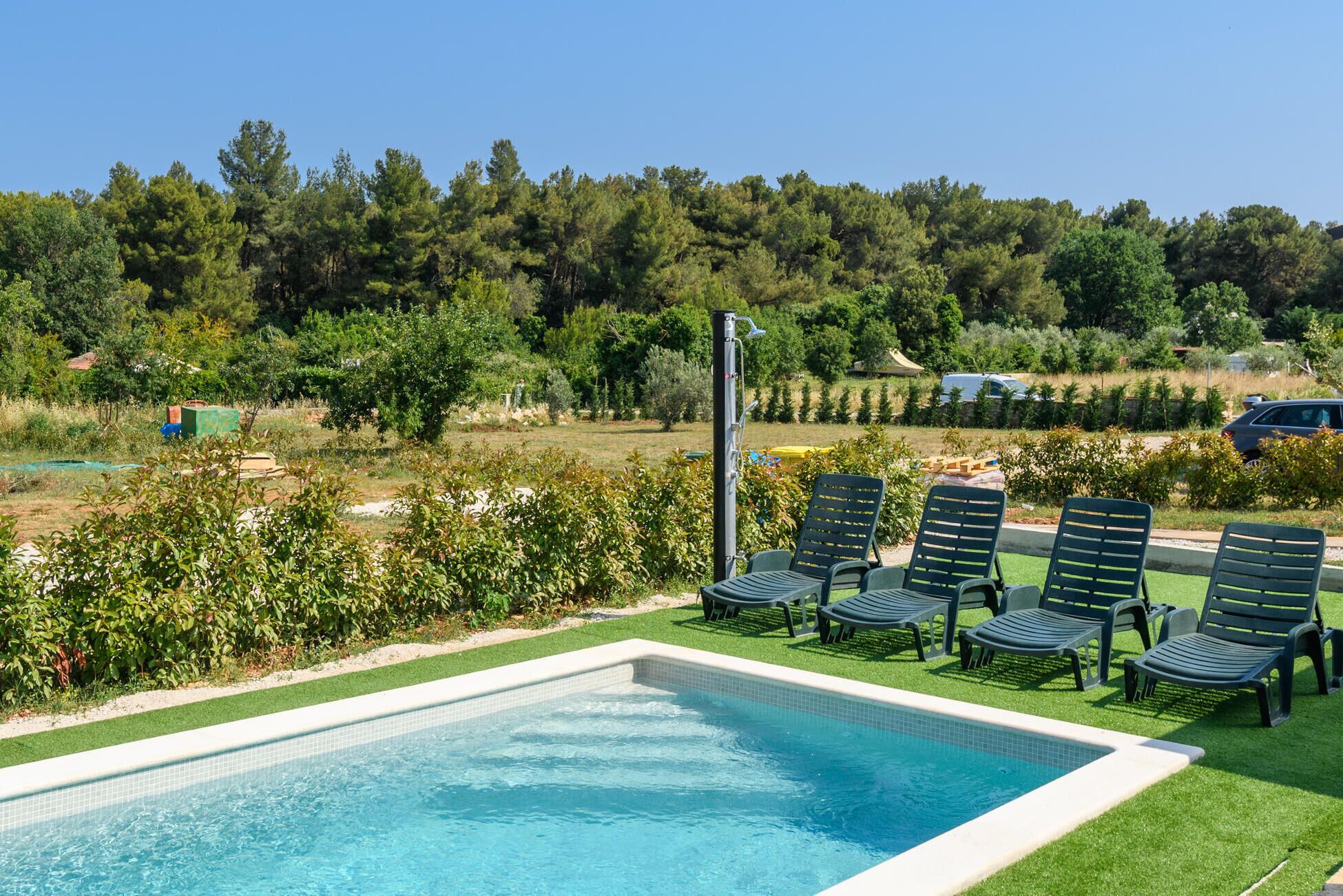 A swimming pool with a tiled edge, surrounded by green lawn and a row of black lounge chairs.