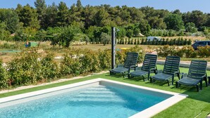 Una piscina con borde de azulejos, rodeada de césped verde y una fila de sillas reclinables negras.