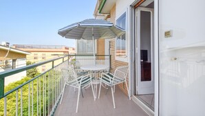 Ein Balkon mit Tisch und Stühlen, einem gestreiften Sonnenschirm und Blick auf benachbarte Gebäude.