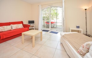 A room with a red sofa, a wooden table, a bed, a TV, and a sliding glass door leading to an outdoor area. - Lovely home in Aigues-Mortes with house sea view (Aigues-Mortes)