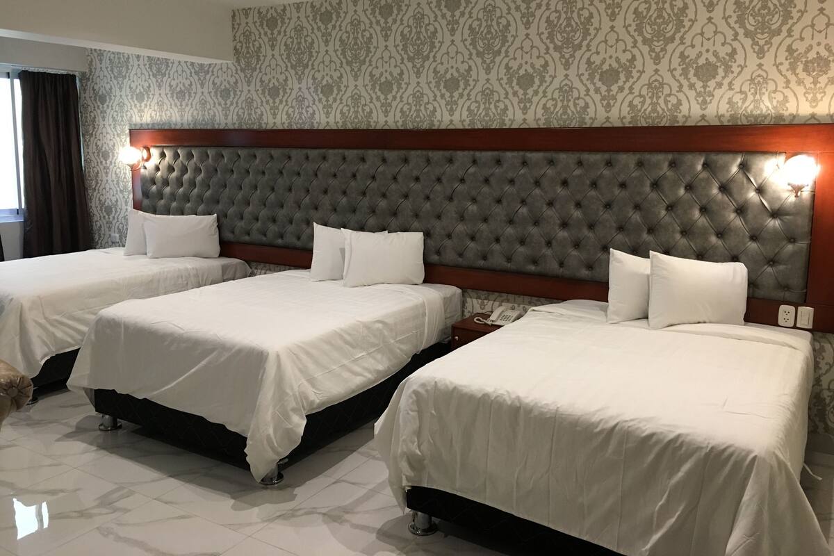 A hotel room with three beds, a tufted headboard, a patterned wallpaper, and a bedside telephone.