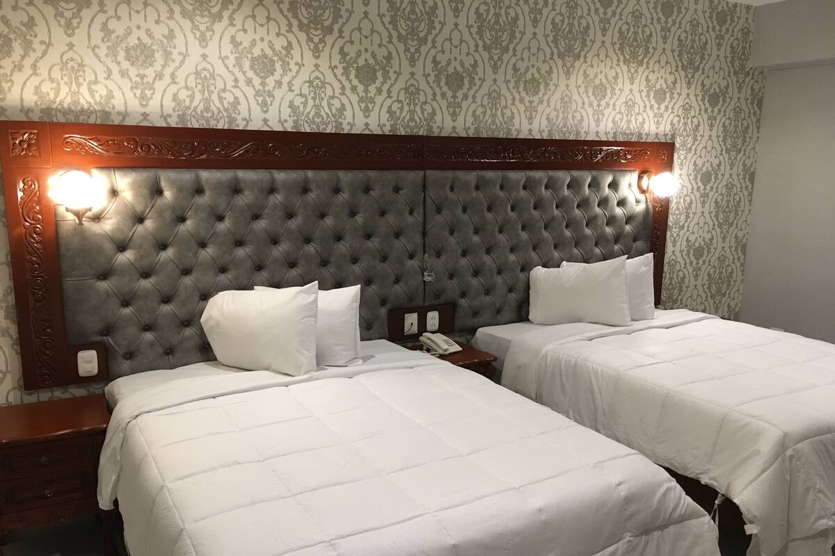 A hotel room with two beds, a tufted headboard, a bedside telephone, and a nightstand.