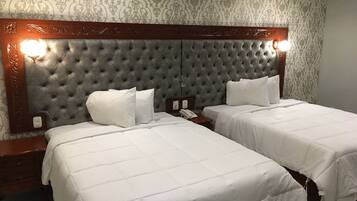 Una habitación de hotel con dos camas, cabecero capitonado, teléfono en la mesita de noche y una mesita.