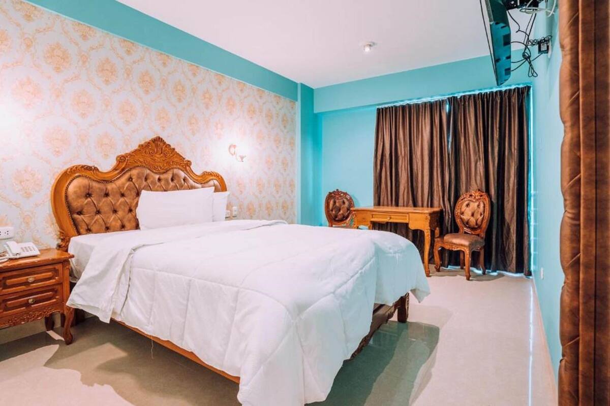A bedroom with a large bed, a wooden nightstand, a desk, and a chair.