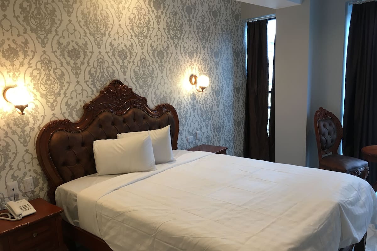 A neatly made bed with a wooden headboard, a bedside telephone, and a wall-mounted light fixture.