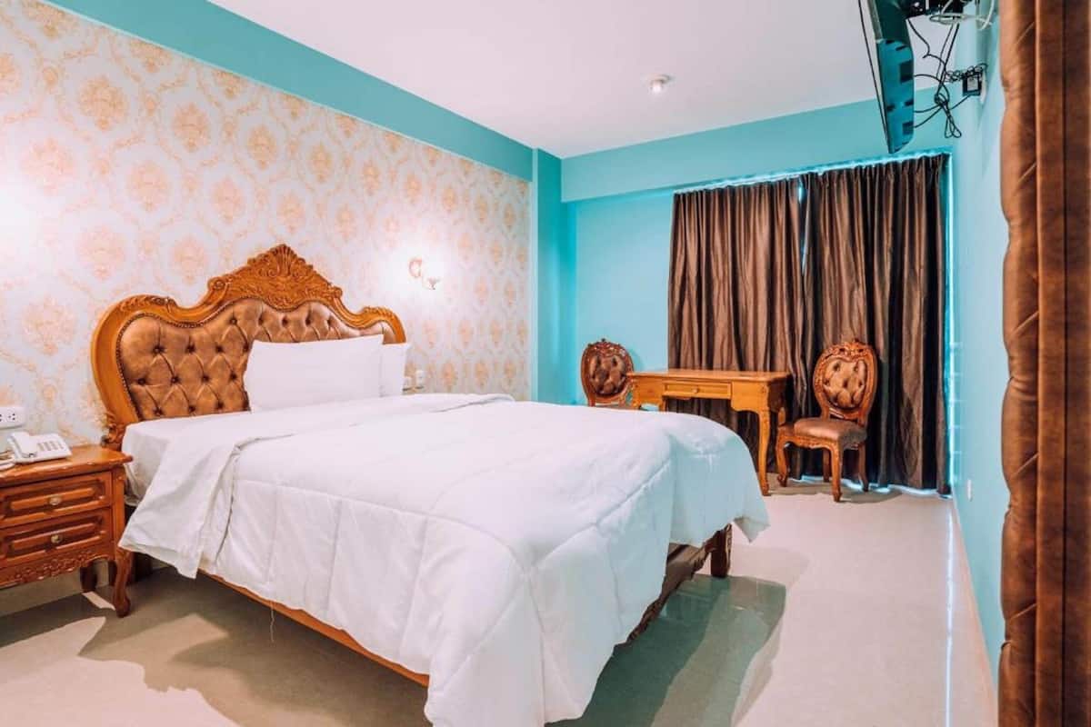 A bedroom with a large bed, a wooden nightstand, a desk, and a chair.