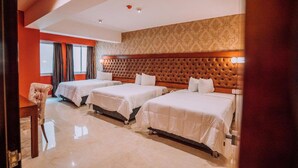 Une chambre d’hôtel avec trois lits, une grande fenêtre avec des rideaux et un mur décoré d’un motif.