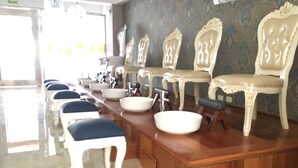 Une rangée de chaises blanches rembourrées, dotées de dossiers décoratifs, un comptoir en bois avec des éviers et un mur orné de motifs dans une pièce.