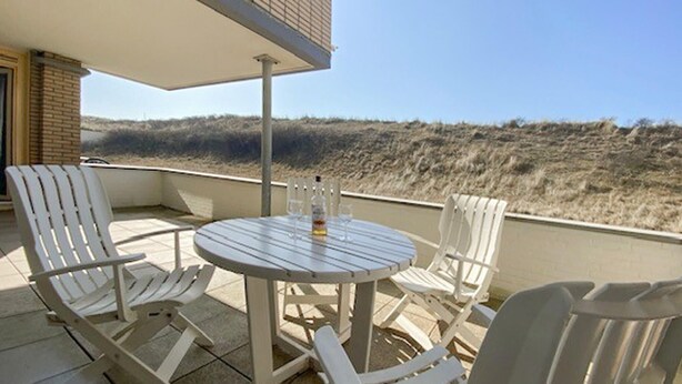A round table with four white chairs on a balcony with a view of a grassy landscape. - Stunning apartment in Bergen aan Zee (Bergen aan Zee)