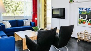 A modern living room with a blue sofa, black chairs, a wooden coffee table, and a TV mounted on the wall. - Stunning apartment in Bergen aan Zee (Bergen aan Zee)