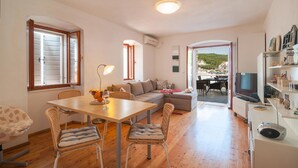Una sala de estar acogedora con comedor, sofá y televisor. Cuenta con un balcón con vistas a la ciudad.