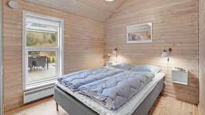 A bedroom with a large window, a bed with blue bedding, two bedside lamps, and a framed picture on the wall. - Amazing home in Væggerløse with sauna (Væggerløse)