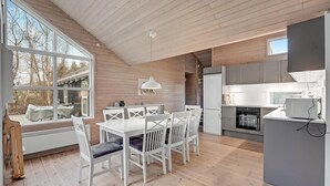 A modern kitchen with white cabinetry, a dining area with white chairs and a table, and a large window overlooking a backyard. - Amazing home in Væggerløse with sauna (Væggerløse)