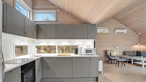 A modern kitchen with grey cabinets, a central island, and a dining area with a sofa and table. - Amazing home in Væggerløse with sauna (Væggerløse)