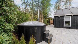 A hot tub with a black exterior, surrounded by greenery and a wooden deck. - Amazing home in Væggerløse with sauna (Væggerløse)