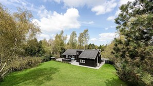 A modern two-story cabin with a sloped roof, surrounded by a well-maintained lawn and dense trees. - Amazing home in Væggerløse with sauna (Væggerløse)