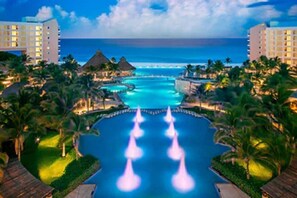 A resort with a large infinity pool, palm trees, and a view of the ocean. - Perfection at the Beach (Cancún)