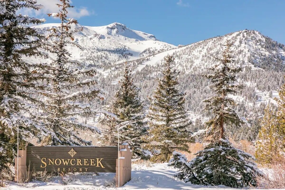 Een bordje voor Snow Creek Resort, omringd door met sneeuw bedekte bomen en bergen.