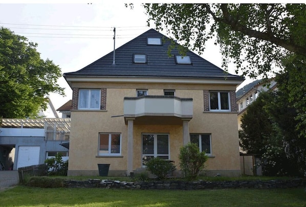 Une maison à deux étages avec un balcon, un garage et un mur de pierre à l’avant.