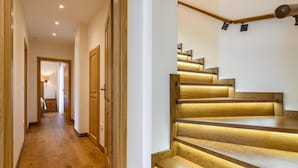 Una escalera de madera con iluminación empotrada, suelo de madera y un pasillo que conduce a una habitación con cama y mesita de noche.
