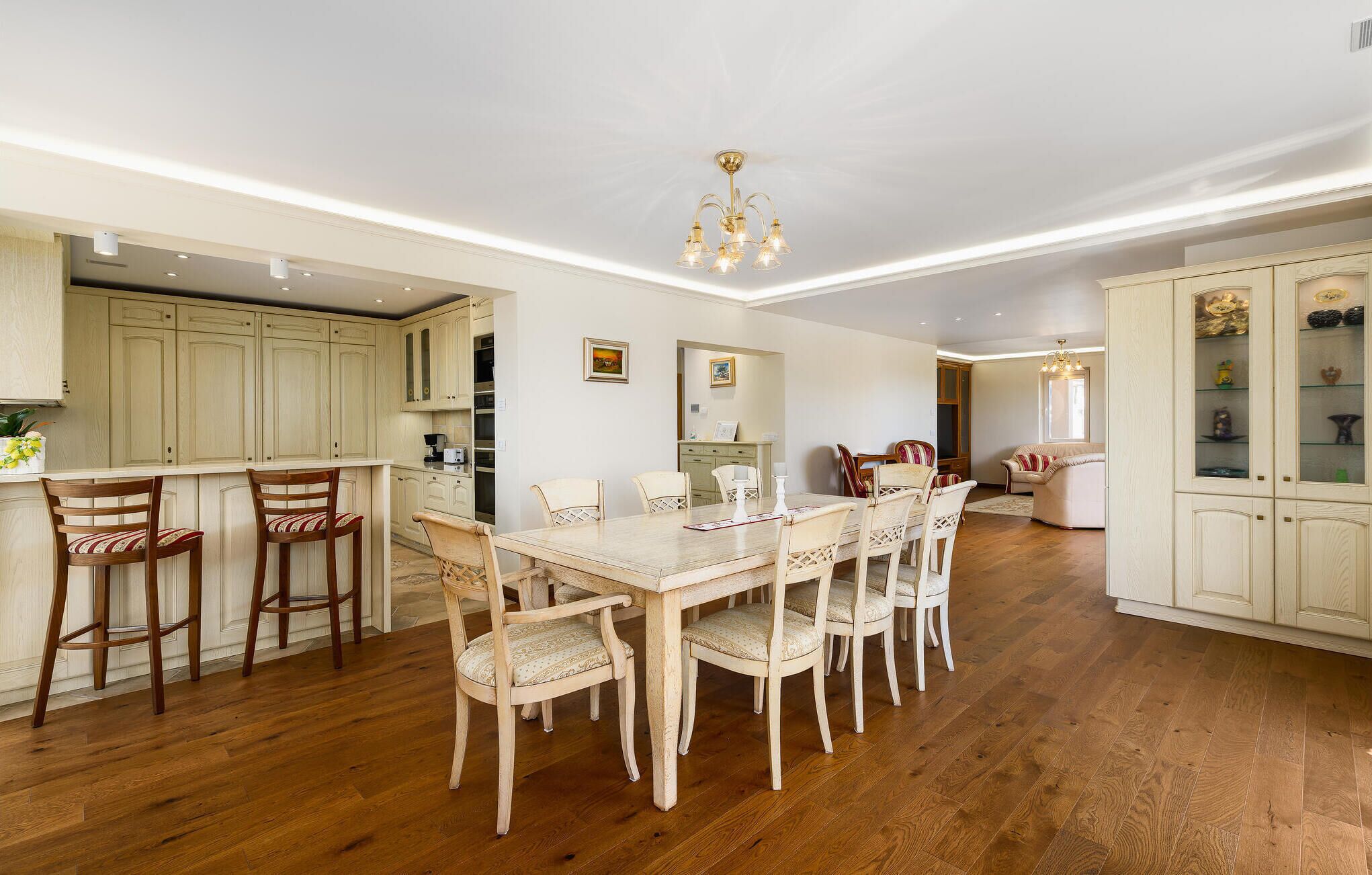 A spacious dining area with a wooden table and chairs, a kitchen with light-colored cabinets, and a chandelier.