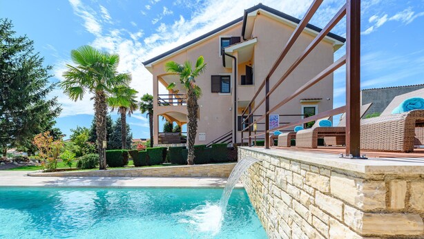 Un edificio moderno con piscina, palmeras y mobiliario para exteriores.