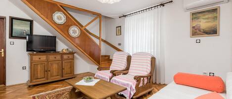 Une pièce avec un escalier en bois, une télévision, un lit avec un oreiller orange, une table en bois et un tapis à motifs.