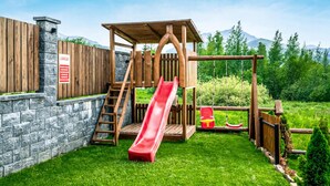 A wooden play structure with a slide, a climbing ladder, and a small swing set. - Beautiful apartment in Koscielisko with sauna (Koscielisko)